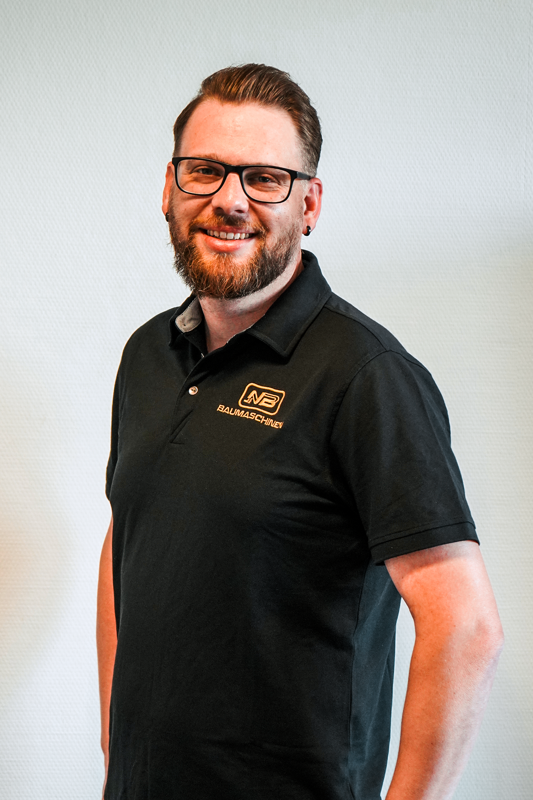 Ein lachender Mensch mit einem schwarzem polo shirt mit dem Firmenlogo von nb baumaschinen.